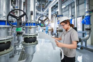 Industrial engineer inspecting valve schematics inside a bulk material handling facility, surrounded by rotary valves and piping systems.