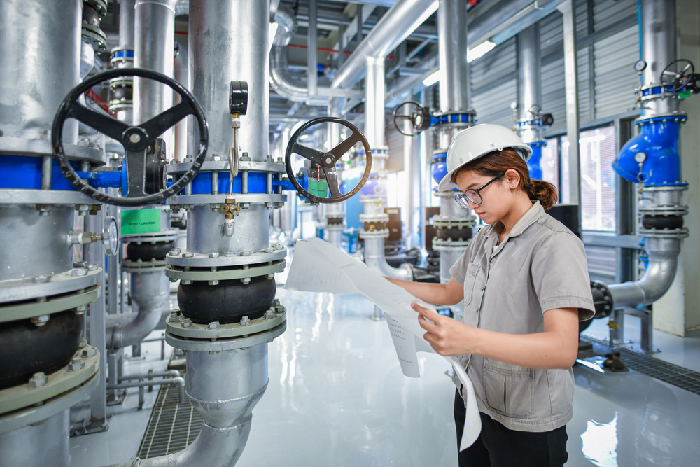 Industrial engineer inspecting valve schematics inside a bulk material handling facility, surrounded by rotary valves and piping systems.