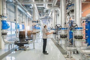 Mechanical engineer in safety gear reviewing system blueprints in an industrial facility, representing precision planning for valve and material handling systems.