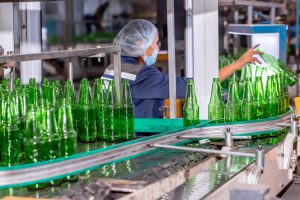 Glass manufacturing plant worker monitoring production line with green glass bottles, bulk material handling system in operation