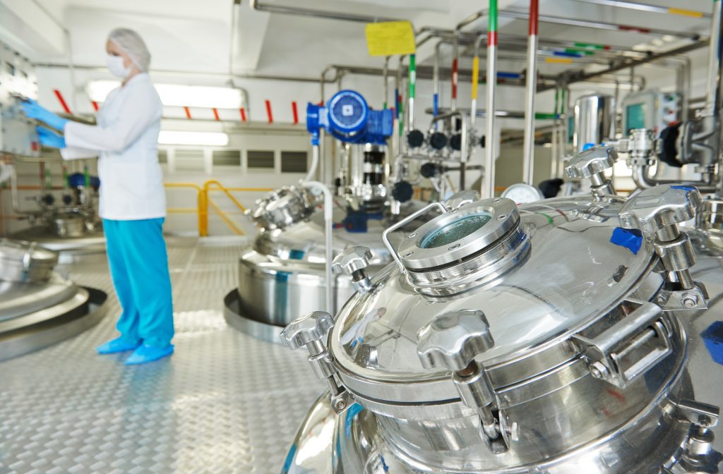Pharmaceutical technician monitoring sanitary airlock valves and stainless steel tanks in facility